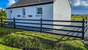 Une maison blanche avec un toit foncé, une clôture en bois et une allée gravillonnée.