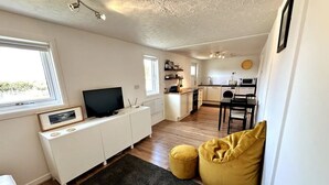 Un espace de vie compact comprenant un coin cuisine, un coin repas et un espace détente avec des coussins.