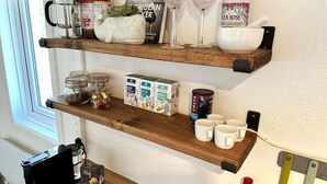 Une cuisine avec des étagères en bois où sont rangés divers objets, comme des bocaux, des boîtes et des ustensiles de cuisine.