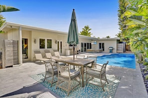 A pool area with a table and chairs, a covered umbrella, and a pool.