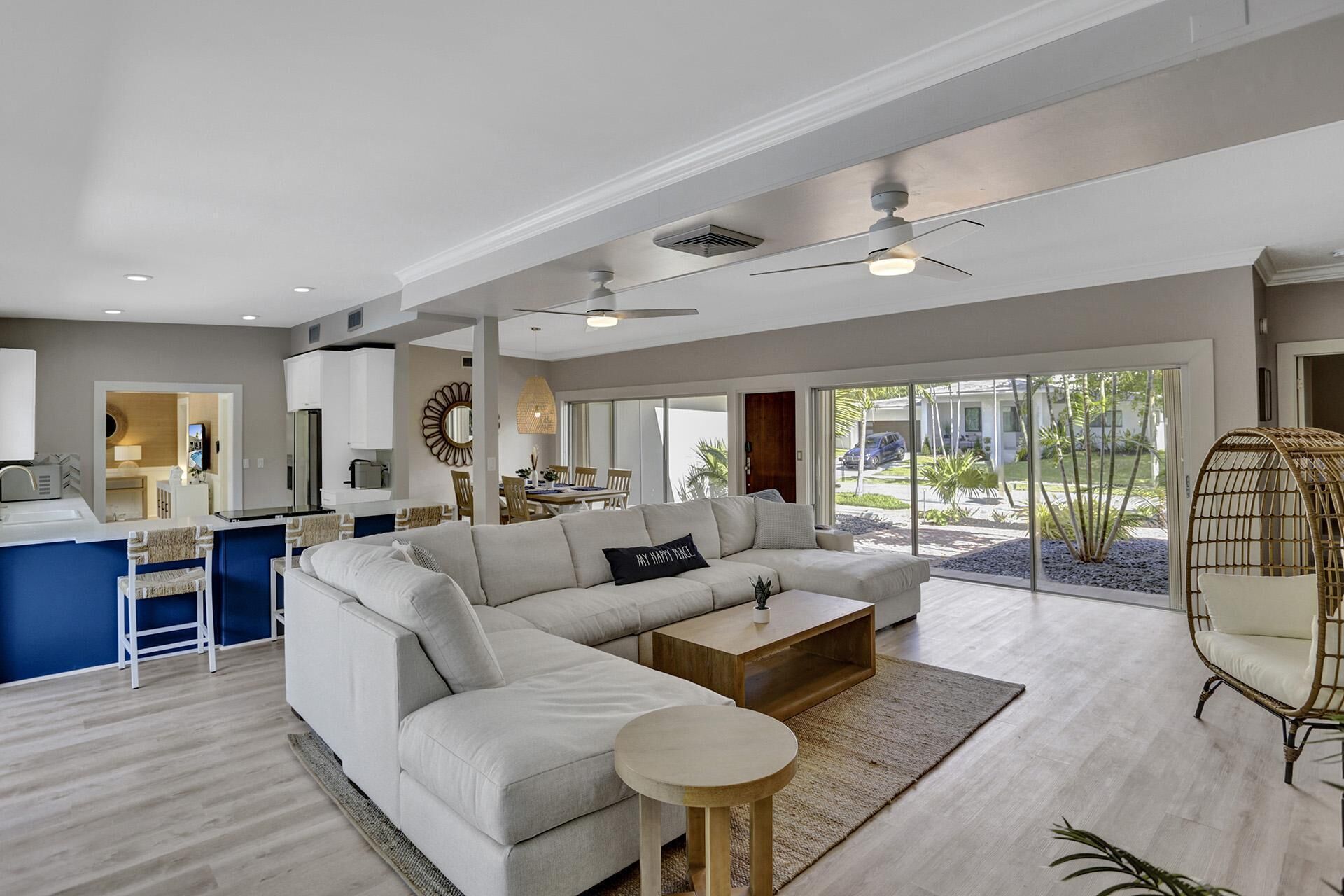 A spacious living area with a large sofa, a coffee table, and a round side table. There is a dining area in the background with a table and chairs.