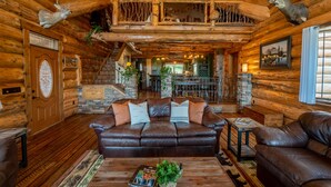 L’intérieur d’une cabane en rondins, avec un canapé en cuir marron, une table à manger et un escalier menant à une mezzanine.