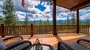 Une terrasse en bois, agrémentée de chaises et d’une table en osier, qui offre une vue sur un paysage montagneux.