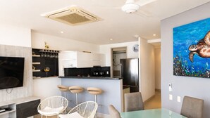 A modern living room with a TV, white rocking chairs, a glass dining table, and a kitchen in the background. - U-GO Edificio Murano Elite, Bocagrande (Cartagena)