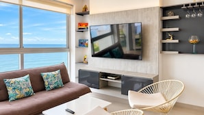 A modern living room with a large TV, a sofa with patterned cushions, a coffee table, and two wicker chairs. - U-GO Edificio Murano Elite, Bocagrande (Cartagena)
