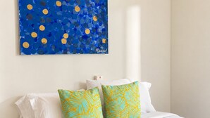 A hotel room with a bed, white bedding, two decorative pillows with a leaf pattern, a wall-mounted artwork with blue and yellow circles, and a white nightstand. - U-GO Edificio Murano Elite, Bocagrande (Cartagena)