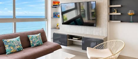 Una sala de estar moderna con un televisor grande, un sofá con cojines estampados, una mesa de centro y dos sillas de mimbre.