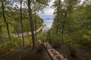 A forested area with a wooden boardwalk leading to a dock by a calm lake.