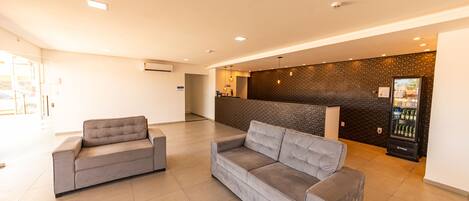 A spacious lobby with two grey sofas, a reception desk, a patterned wall, and a vending machine.