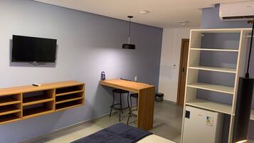 A room with a bed, a desk, a TV, and a mini-fridge.