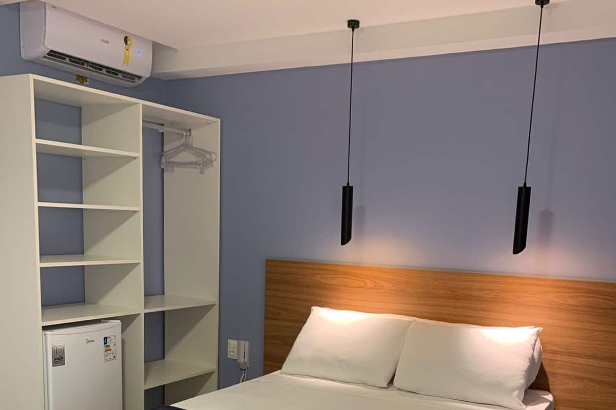 Ein ordentlich bezogenes Bett mit Holz Kopfteil, einer weißen und dunkelblauen Tagesdecke sowie zwei Pendelleuchten darüber.