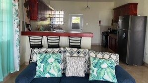 A compact living space with a kitchenette, a dining area with a bar, and a sofa with patterned cushions. - Tranquil 2-bedroom apartment in Beautiful Barbados (Saint Philip)