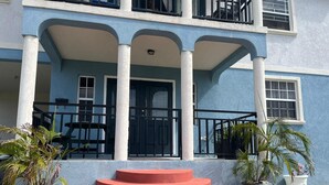 A two-story building with a blue facade, a central entrance with a black door, and a red staircase leading to the entrance. - Tranquil 2-bedroom apartment in Beautiful Barbados (Saint Philip)