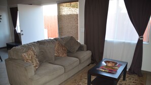 Ein Wohnzimmer mit einem beigen Sofa, einem kleinen Tisch und einem Fenster mit Vorhängen.