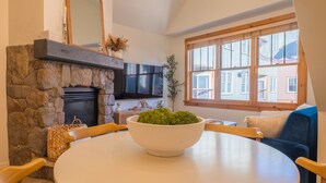 A dining area with a stone fireplace, a large white bowl on the table, and a window with a view of buildings. - Remodeled modern ski-in/ ski-out condo in Keystone, 1 bd/1 ba, sleeps 4 (Keystone)