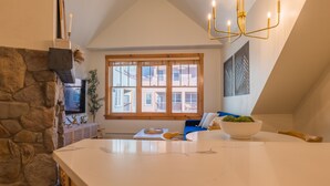A modern kitchen with a stone wall, a large window, and a dining area with a white table and blue sofa. - Remodeled modern ski-in/ ski-out condo in Keystone, 1 bd/1 ba, sleeps 4 (Keystone)
