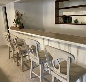 Une cuisine avec un plan de travail blanc, quatre chaises en bois et un grand miroir au-dessus du plan de travail.