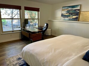 Une chambre à coucher avec un lit, un bureau avec une chaise, une fenêtre et des œuvres d’art accrochées au mur.