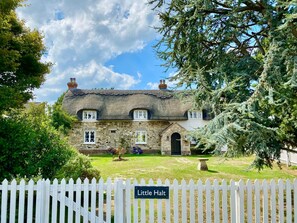 A traditional stone cottage with a thatched roof, a white picket fence, and a sign reading "Little Halt".