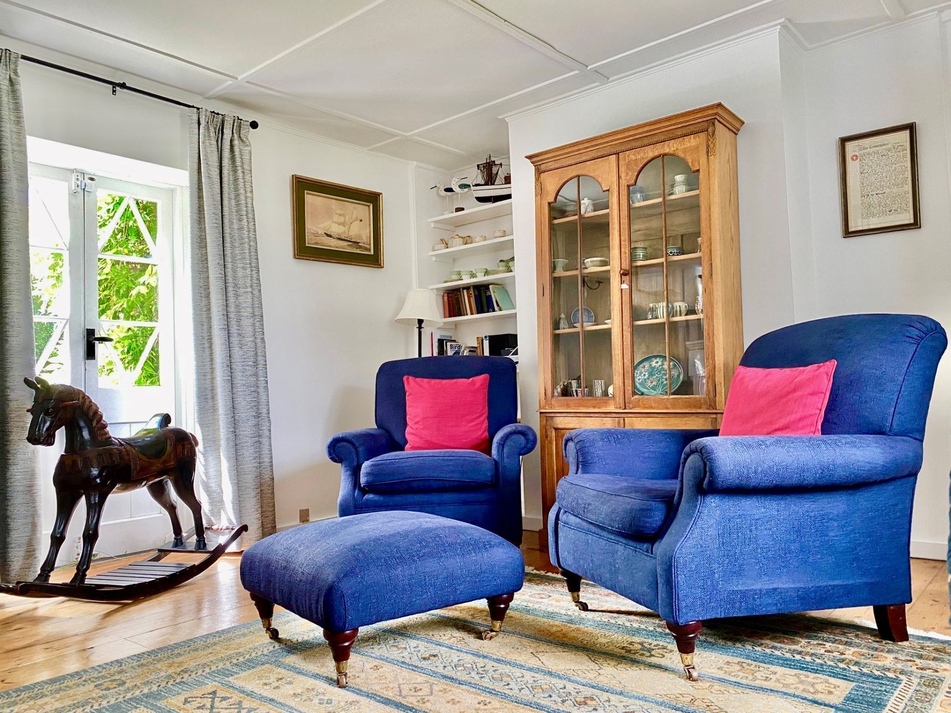 A room with two blue armchairs, a wooden cabinet with glass doors, and a rocking horse.