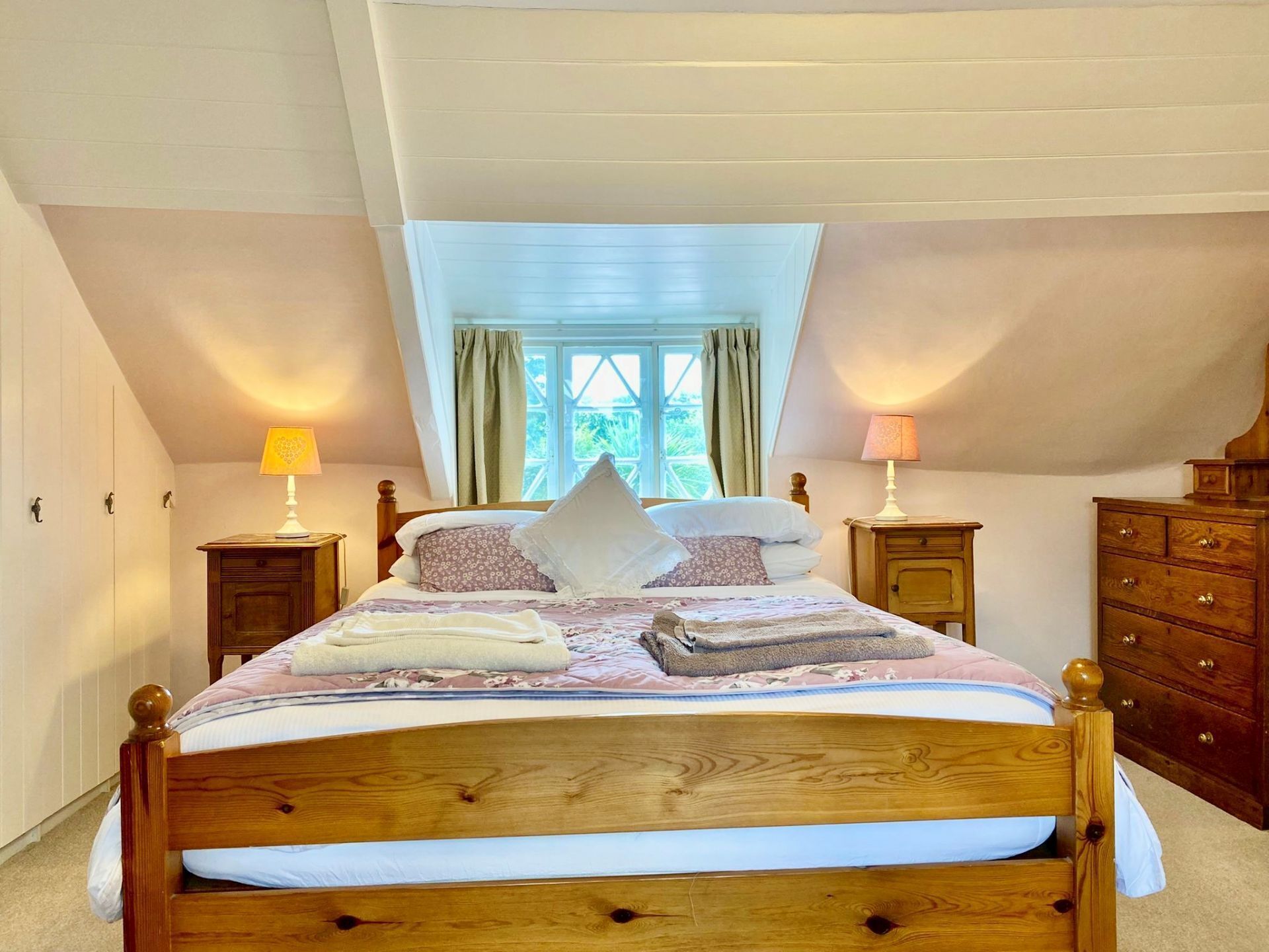 Une chambre à coucher avec un lit en bois, deux tables de chevet avec des lampes, une commode et une fenêtre avec des rideaux.