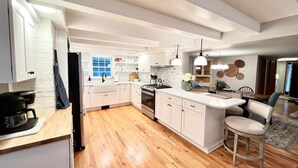 Una cocina moderna con armarios blancos, una isla central y una zona de comedor con un taburete de bar.