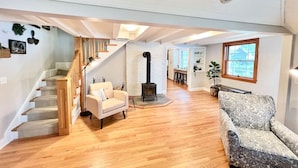 Un amplio salón con una escalera, un sofá, un sillón estampado, una chimenea y una ventana con vistas.