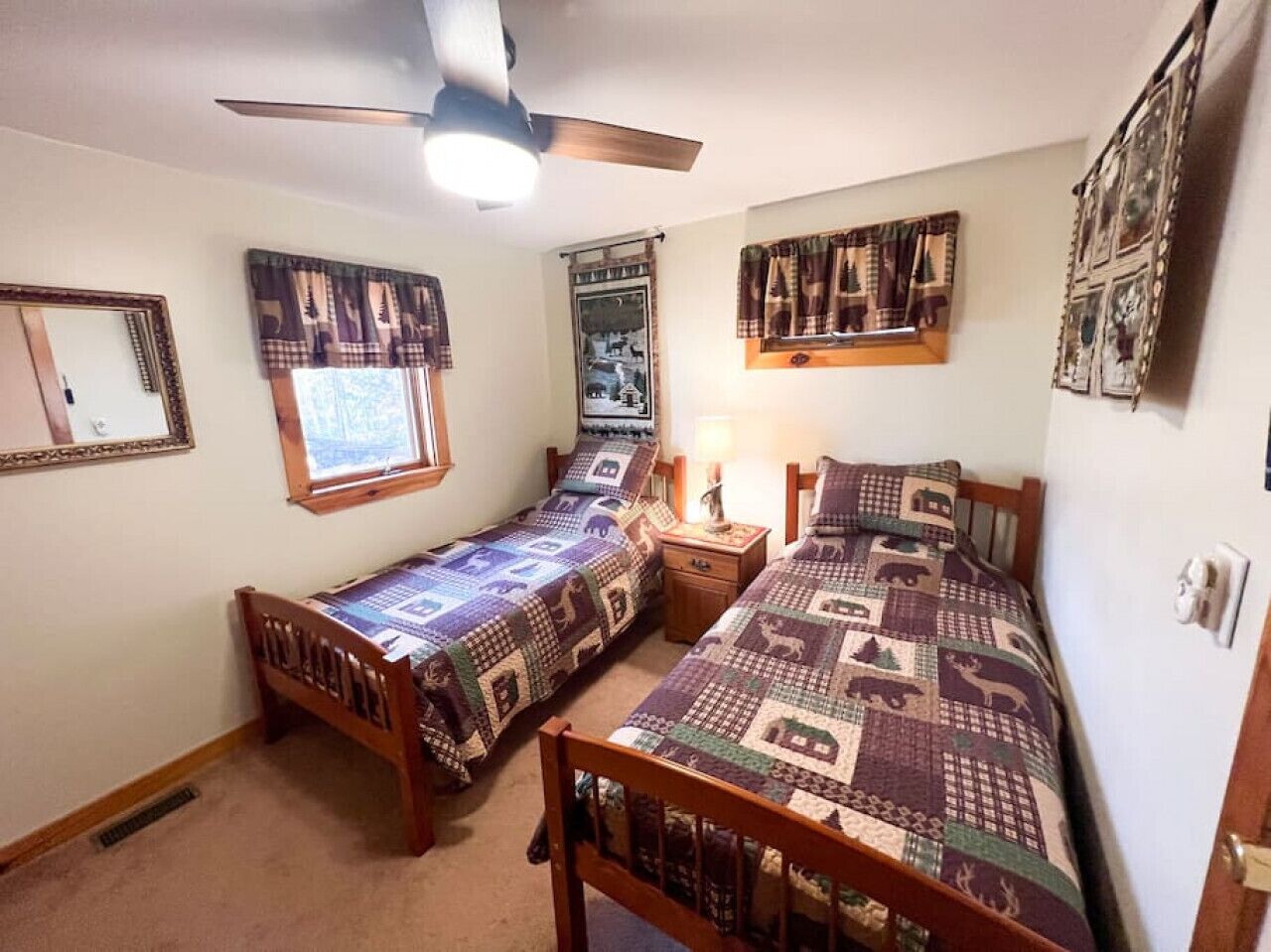 A bedroom with two single beds, a ceiling fan, a window with curtains, and a wall-mounted mirror.