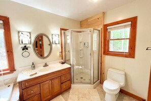 A bathroom with a wooden vanity, a glass shower enclosure, a toilet, and a window with a view of trees. - Cozy Adirondack Mountain Cabin- Inlet, NY - Sleeps 9! (Inlet)