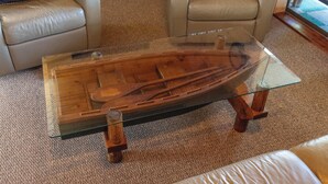 A glass-top coffee table with a wooden boat design, placed on a carpeted floor in a living room with leather sofas. - Catch on the Canal - Waterfront Getaway Near Casino, Dining & Entertainment (Standish)