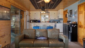 A cozy cabin interior with a wooden ceiling, a dining table with chairs, a kitchen area, and a living room with a leather sofa. - Catch on the Canal - Waterfront Getaway Near Casino, Dining & Entertainment (Standish)