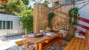 An outdoor dining area with a bamboo fence, a stone floor, and a wooden table set with bowls, glasses, and a bottle. - 1 bedroom stunning apartment in Kosljun (Kosljun)