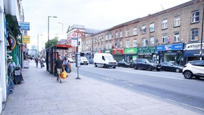 A street with shops, a bus stop, and a white van. - Lovely 1-bedroom condo in Greater London (London)