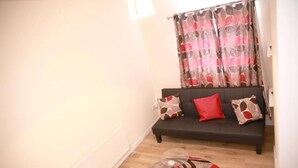 A living room with a dark sofa, patterned cushions, and a patterned curtain. - Lovely 1-bedroom condo in Greater London (London)