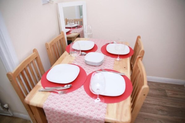 Een eettafel gedekt voor vier personen, met rode placemats, witte borden en wijnglazen.