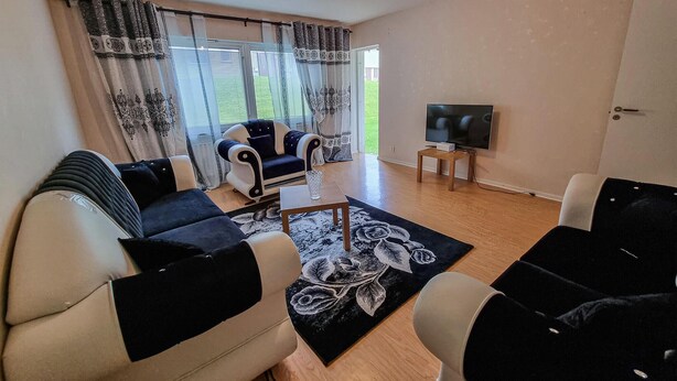 Een woonkamer met een bank, fauteuils, een salontafel, een televisie en een raam met gordijnen.