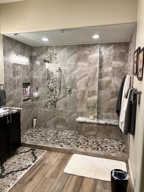 Une salle de bain moderne équipée d’une douche, de carreaux de marbre, d’un meuble-lavabo et d’une petite étagère où sont rangés les articles de toilette.