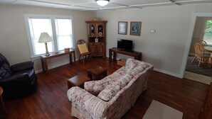 Uma sala de estar com sofá, um armário de madeira, uma televisão e um espaço de jantar com cadeiras.