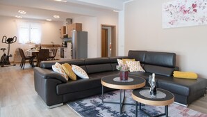 A modern living room with a black leather sofa, two round wooden side tables, and a dining area in the background. - Stunning home in Labin (Labin)