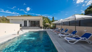 A swimming pool with lounge chairs and umbrellas, a covered seating area, and a building with a door and steps. - Stunning home in Labin (Labin)