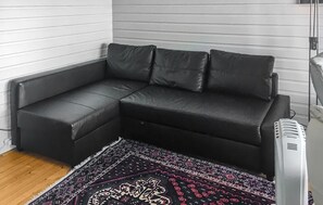 A corner room with a black leather sofa, a patterned rug, and a white wall.