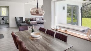 A modern dining area with a wooden table, cushioned chairs, and a hanging light fixture. - 3 bedroom cozy home in Gotlands Tofta (Gotlands Tofta)