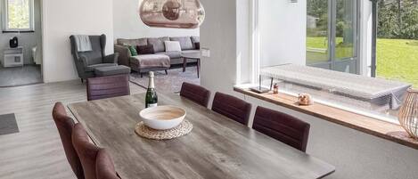 A modern dining area with a wooden table, cushioned chairs, and a hanging light fixture.