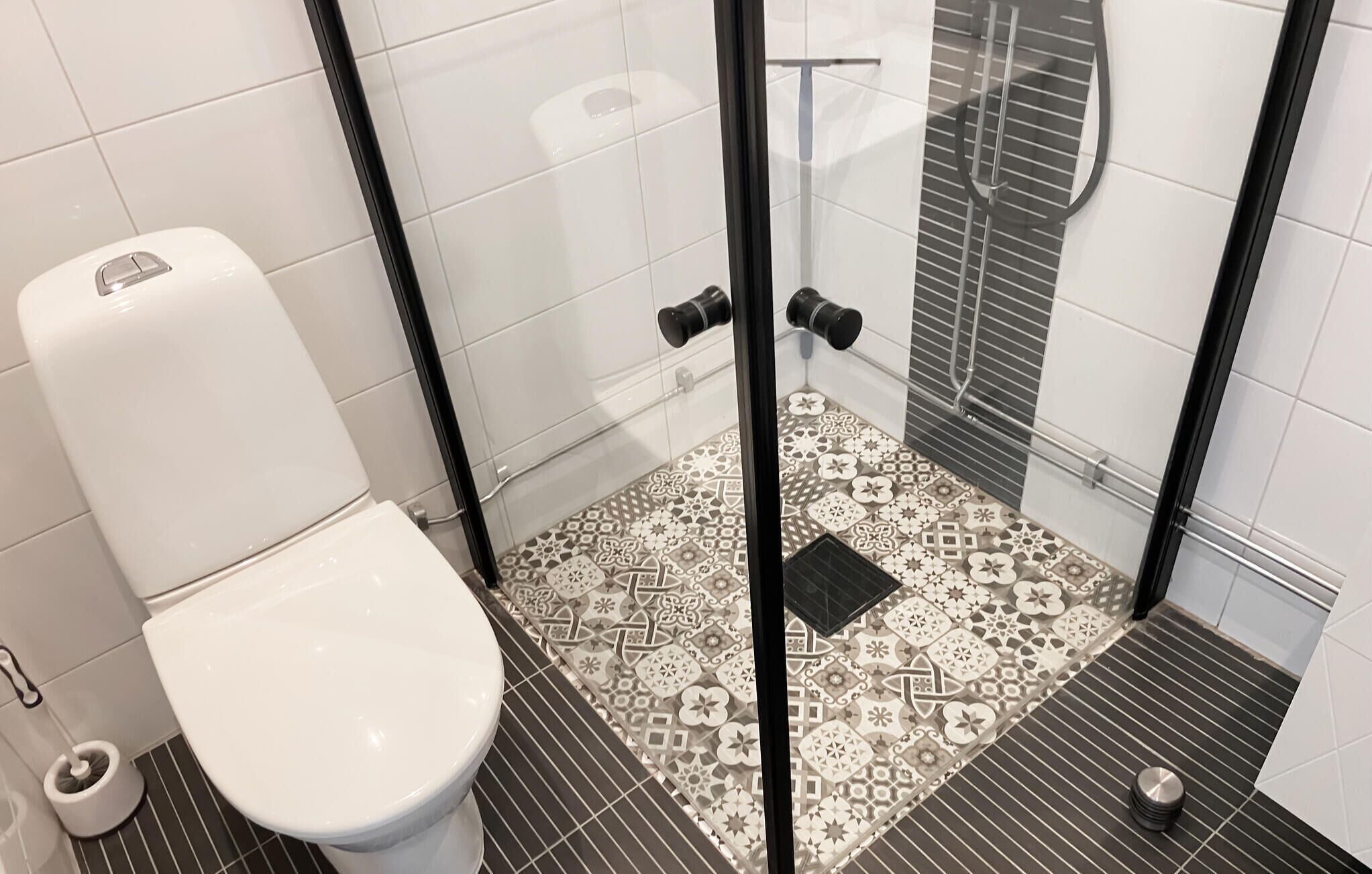 A bathroom with a toilet, a shower with a glass door, and patterned floor tiles.