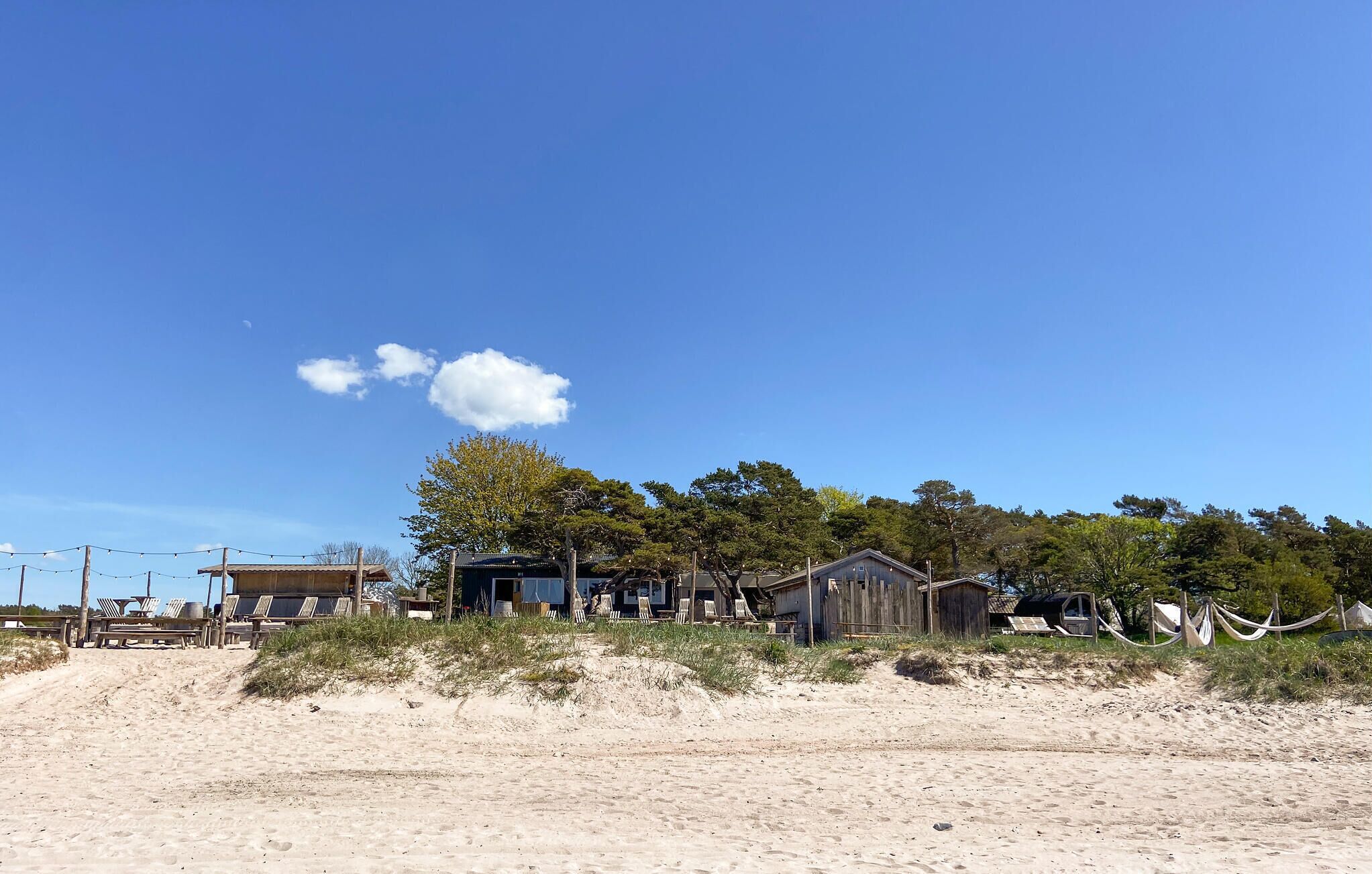 A beachside property with a sandy beach, wooden cabins, and a clear blue sky.