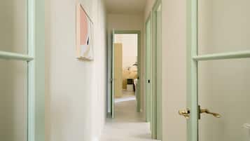 Un pasillo con puertas verde claro, una obra de arte enmarcada en la pared y vistas a una habitación con cama y mesita de noche.