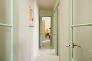 A hallway with light green doors, a framed artwork on the wall, and a view into a room with a bed and a nightstand. - Casa Cosi - Don Bajos (Barcelona)