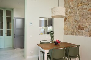 A dining area with a wooden table, four chairs, a hanging light fixture, a stone wall, and a kitchen with a refrigerator and cabinets. - Casa Cosi - Don Bajos (Barcelona)