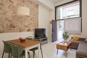 A modern living room with a stone wall, a dining area with a table and chairs, a television, a sofa, and a window with a view of greenery. - Casa Cosi - Don Bajos (Barcelona)