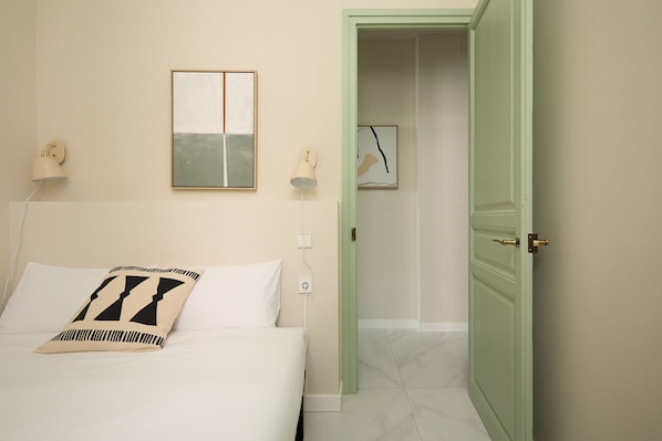 A hotel room with a bed, a nightstand, a wall-mounted lamp, and a door leading to a bathroom. - Casa Cosi - Don Bajos (Barcelona)